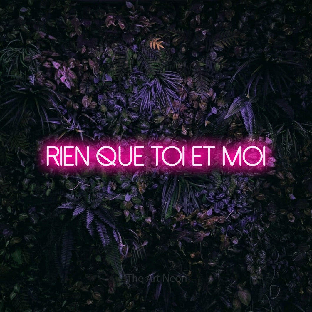 Lettrage en néon LED « Rien que toi et moi » en rose vif, en lettres fines sans empattement, présenté sur un mur sombre aux fleurs violettes, pour un décor romantique.