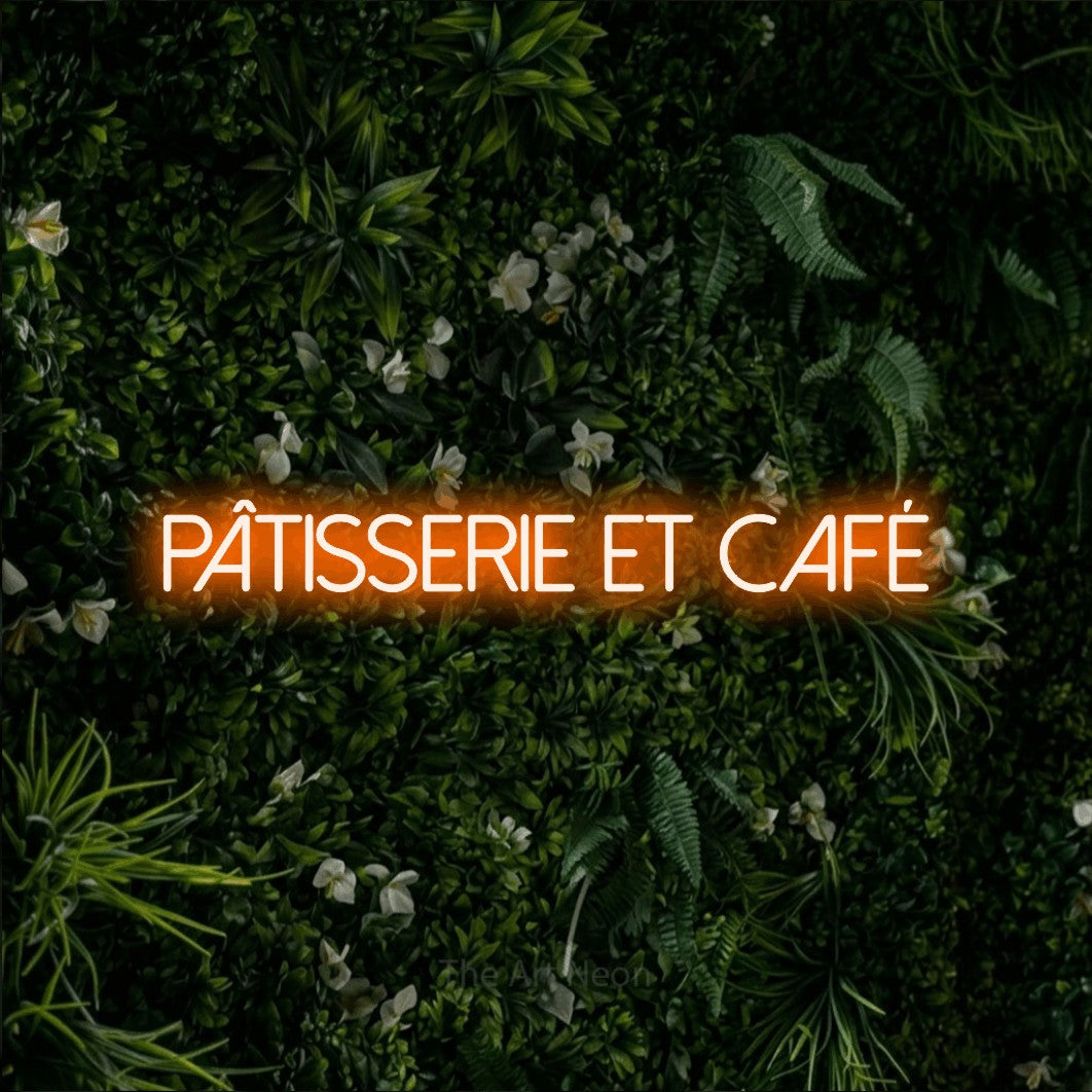 “Pâtisserie et café” LED neon sign in orange, with thin sans-serif lettering, shown against a dense green plant wall.