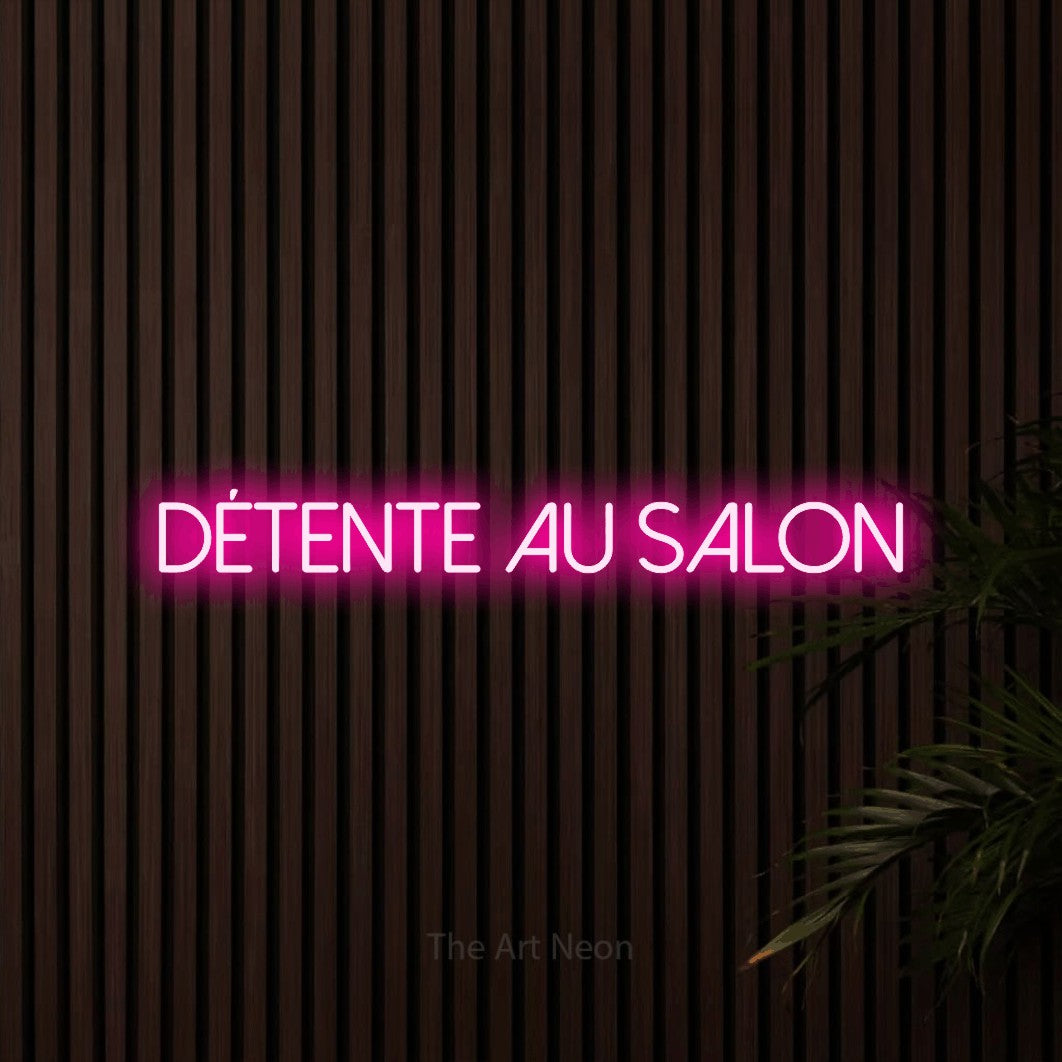 “Détente au salon” LED neon sign in hot pink, with thin sans-serif lettering, shown against dark wooden wall slats.