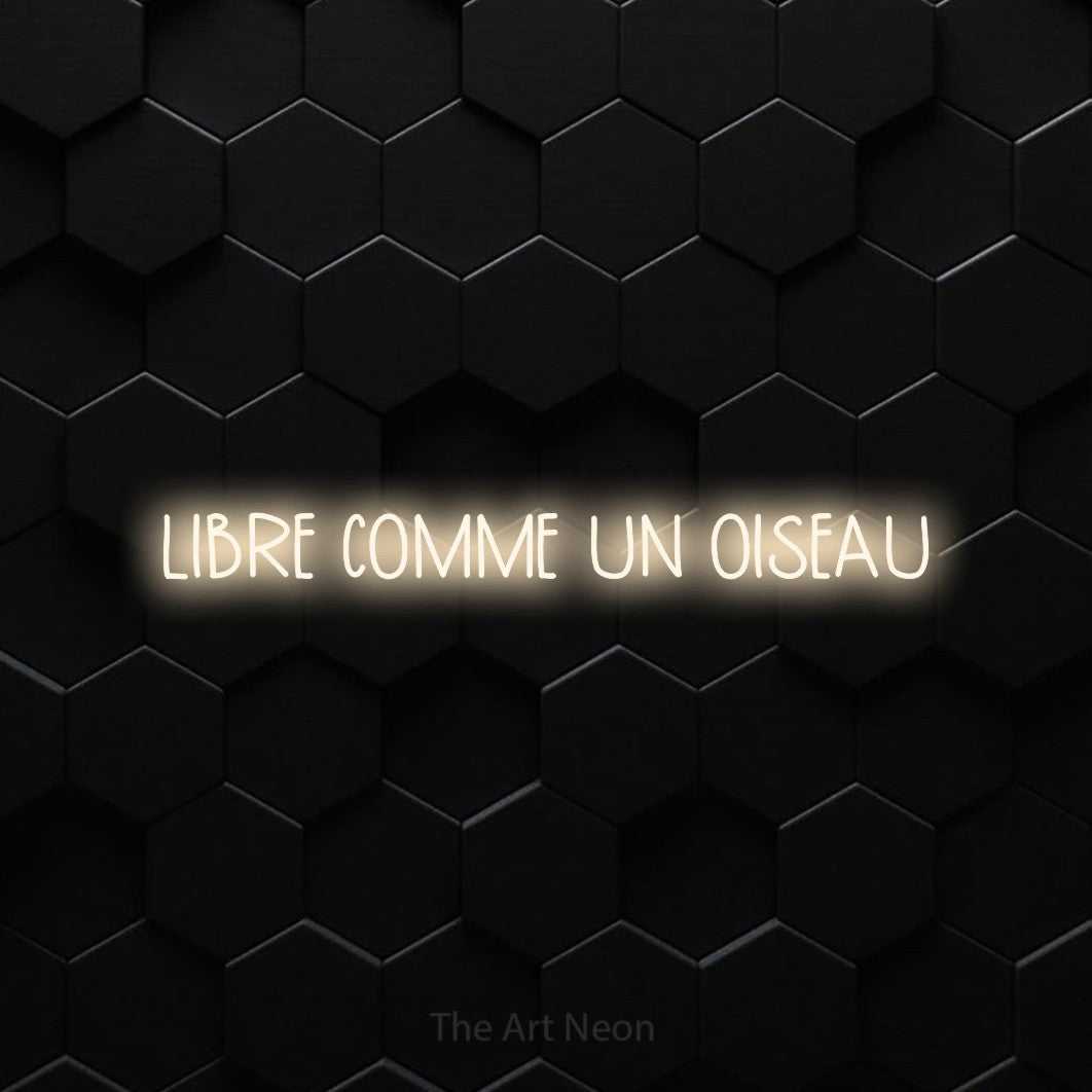 Néon LED « Libre comme un oiseau » en blanc chaud, en lettres étroites dessinées à la main, mis en scène sur un mur de carreaux hexagonaux noirs, pour un décor inspiré de la nature.