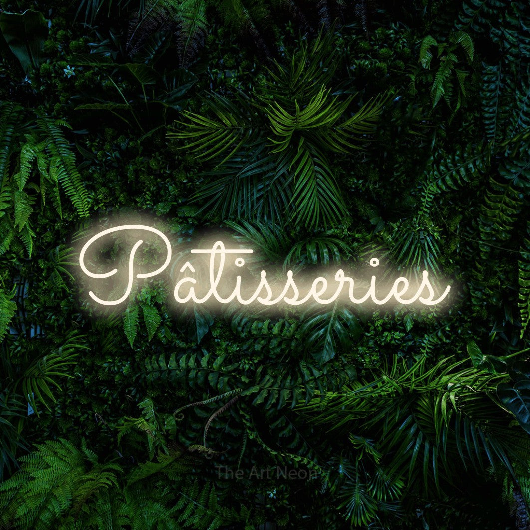 Composition en néon LED « Pâtisseries » en blanc chaud, en lettres cursives aux boucles marquées, mise en valeur devant un feuillage tropical dense, pour un café.