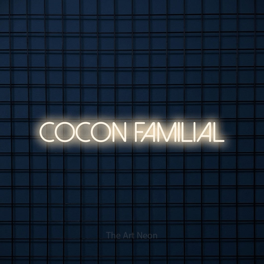 “Cocon familial” LED neon sign in warm white, with thin sans-serif lettering, shown against a dark blue grid.