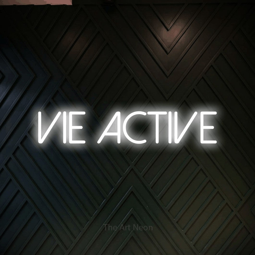 Aperçu d’une enseigne néon LED « Vie active » en blanc froid, en lettres fines sans empattement, photographiée sur un mur en bois noir à motif chevron, pour un espace d’entraînement.