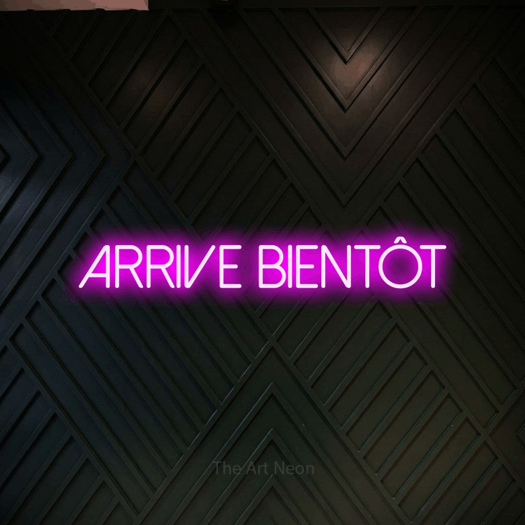 “Arrive bientôt” LED neon sign in pink, with thin sans-serif lettering, shown against a black chevron-patterned wood wall.