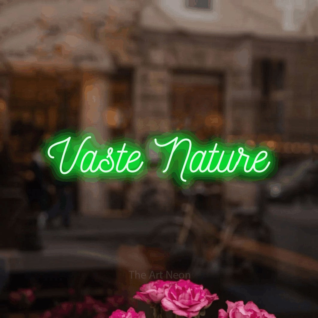 “Vaste nature” LED neon sign in green, with ornate cursive lettering, shown against a blurred café-bar interior.