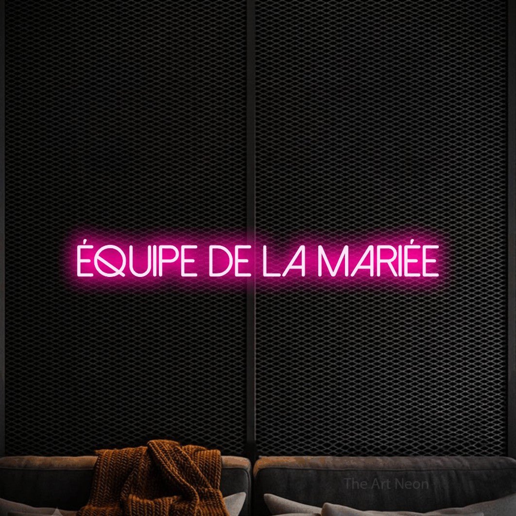 “Équipe de la mariée” LED neon sign in hot pink, with thin sans-serif lettering, shown against a modern dark-toned seating area.