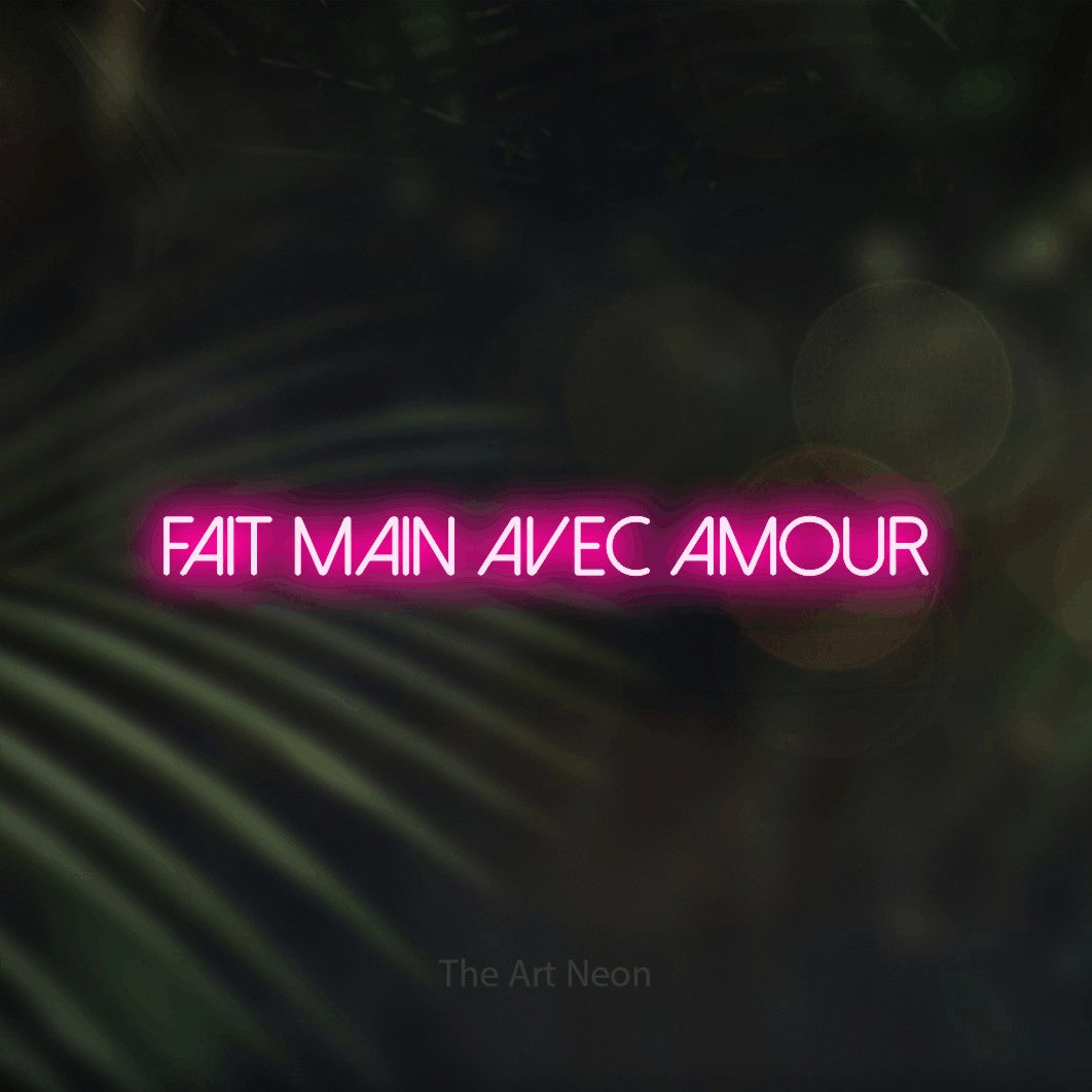 “Fait main avec amour” LED neon sign in hot pink, with thin sans-serif lettering, shown against a blurred palm and bokeh-light backdrop.