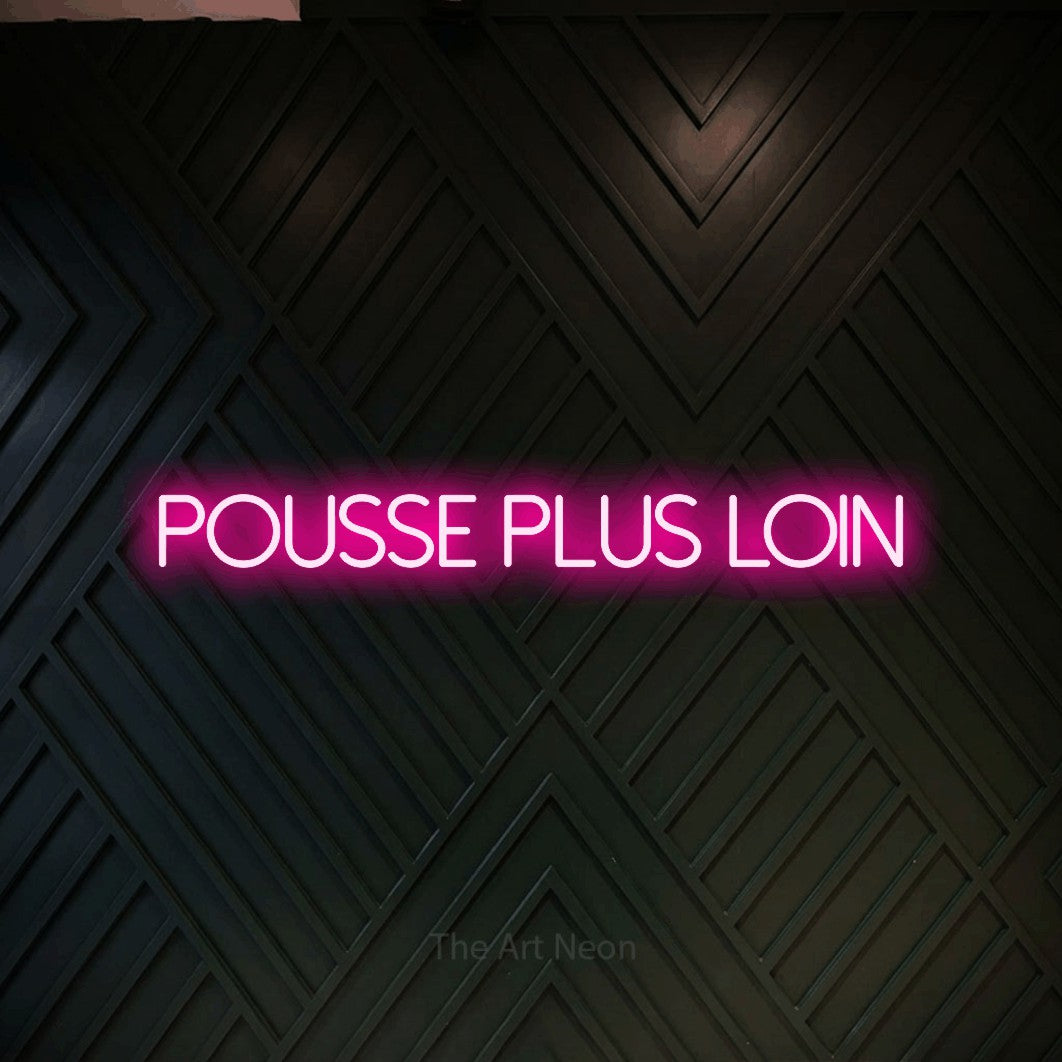 “Pousse plus loin” LED neon sign in hot pink, with thin sans-serif lettering, shown against a black chevron-patterned wood wall.