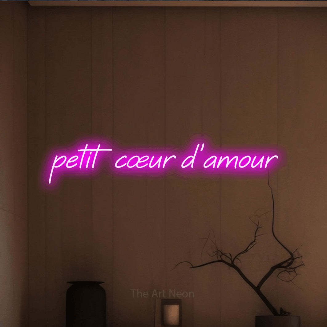 “Petit cœur d'amour” LED neon sign in pink, with slanted cursive lettering, shown against a simple earth-toned interior.