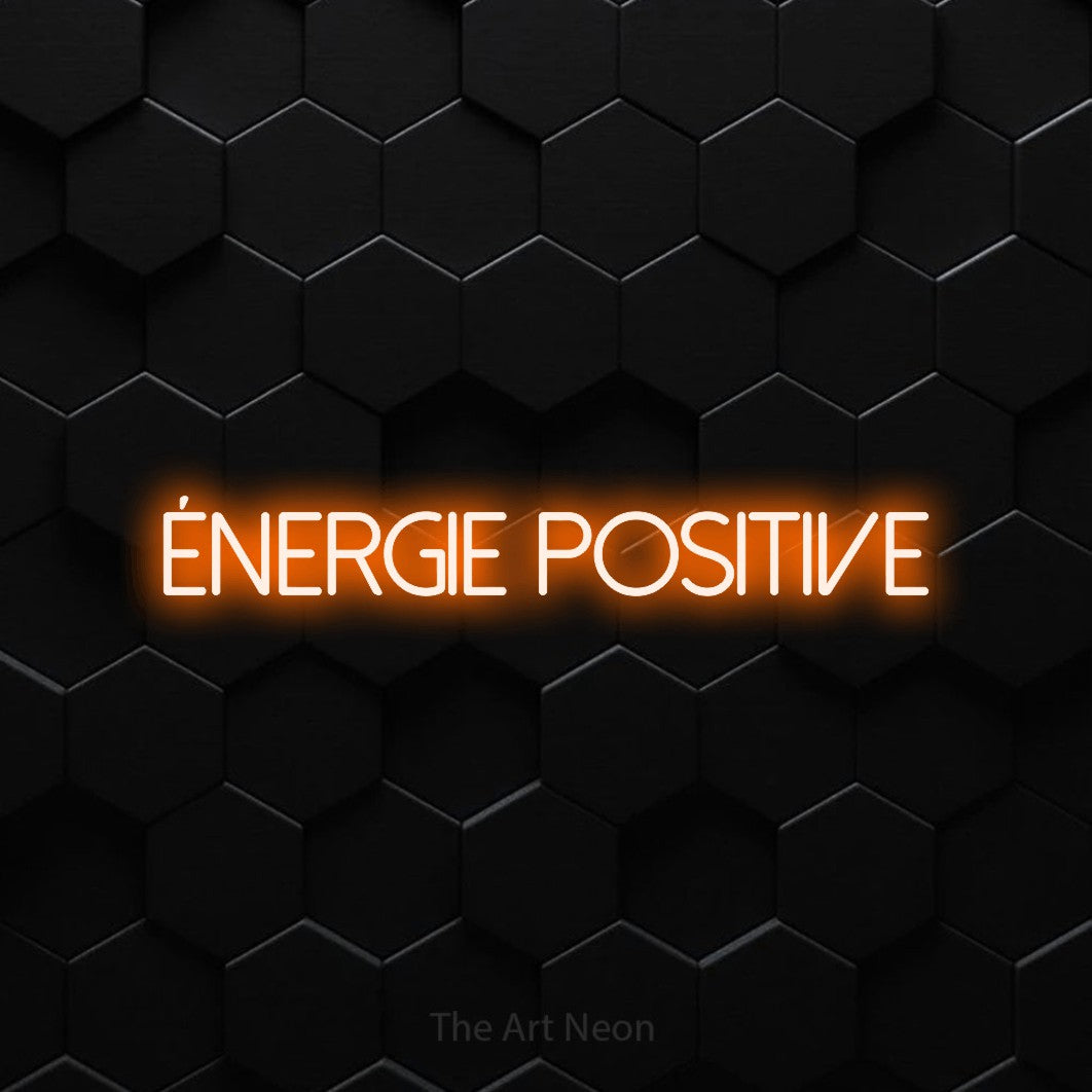“Énergie positive” LED neon sign in orange, with thin sans-serif lettering, shown against black hexagonal wall tiles.