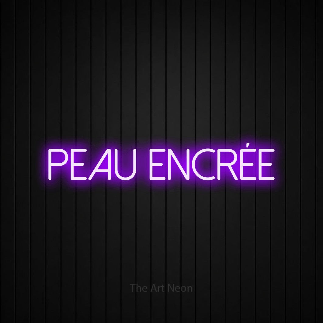 Composition en néon LED « Peau encrée » en violet, en lettres fines sans empattement, mise en valeur sur un mur de lattes verticales noires, pour un studio de tatouage.