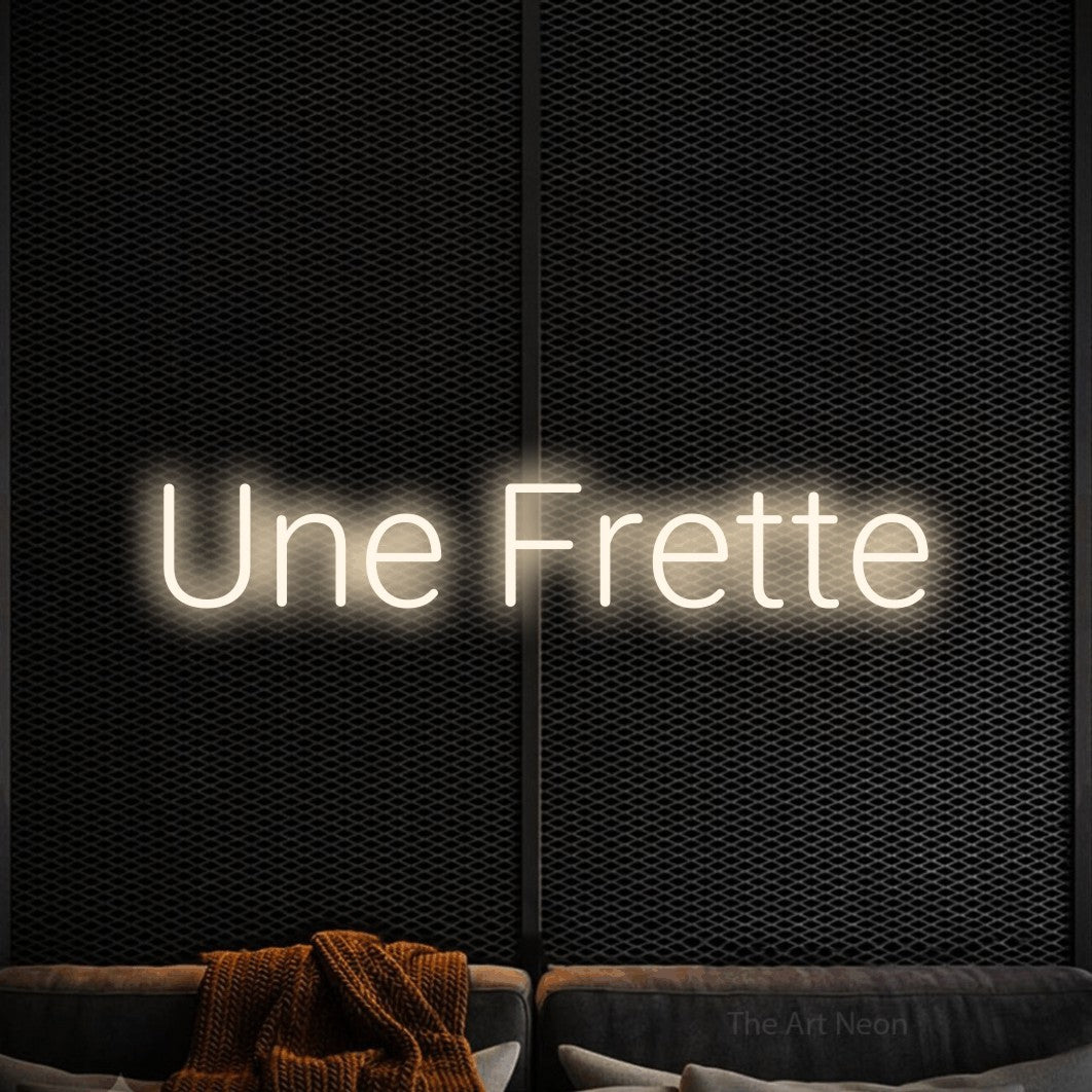 Enseigne néon LED « Une frette » en blanc chaud, en lettres sans empattement arrondies, présentée dans un coin salon moderne aux tons noirs, pour un bar à la maison.