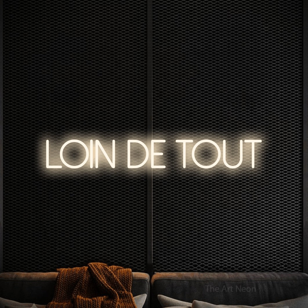 “Loin de tout” LED neon sign in warm white, with thin sans-serif lettering, shown against a modern dark-toned seating area.