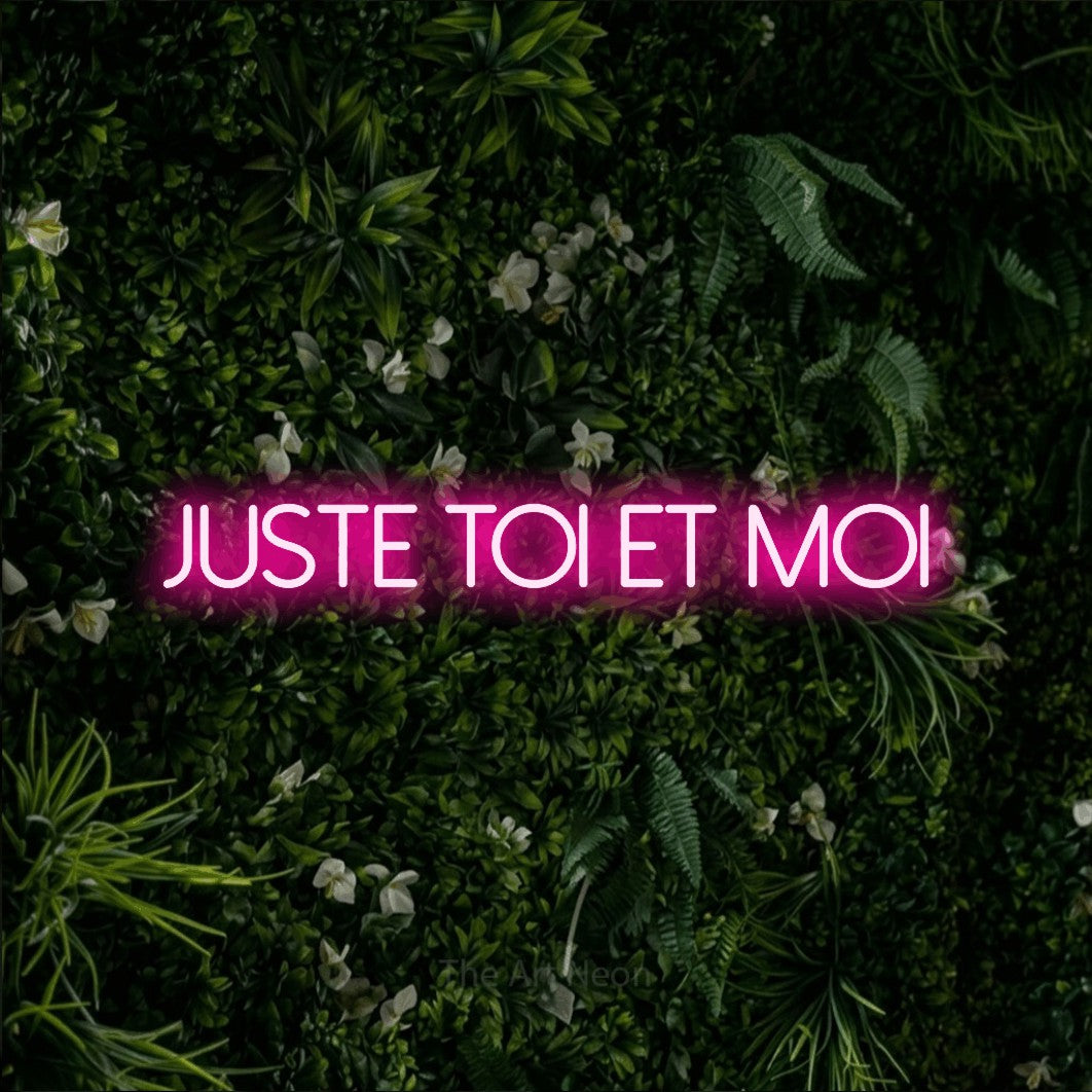 Néon LED « Juste toi et moi » en rose vif, en lettres fines sans empattement, mis en scène sur un mur végétal vert et dense, pour un décor romantique.