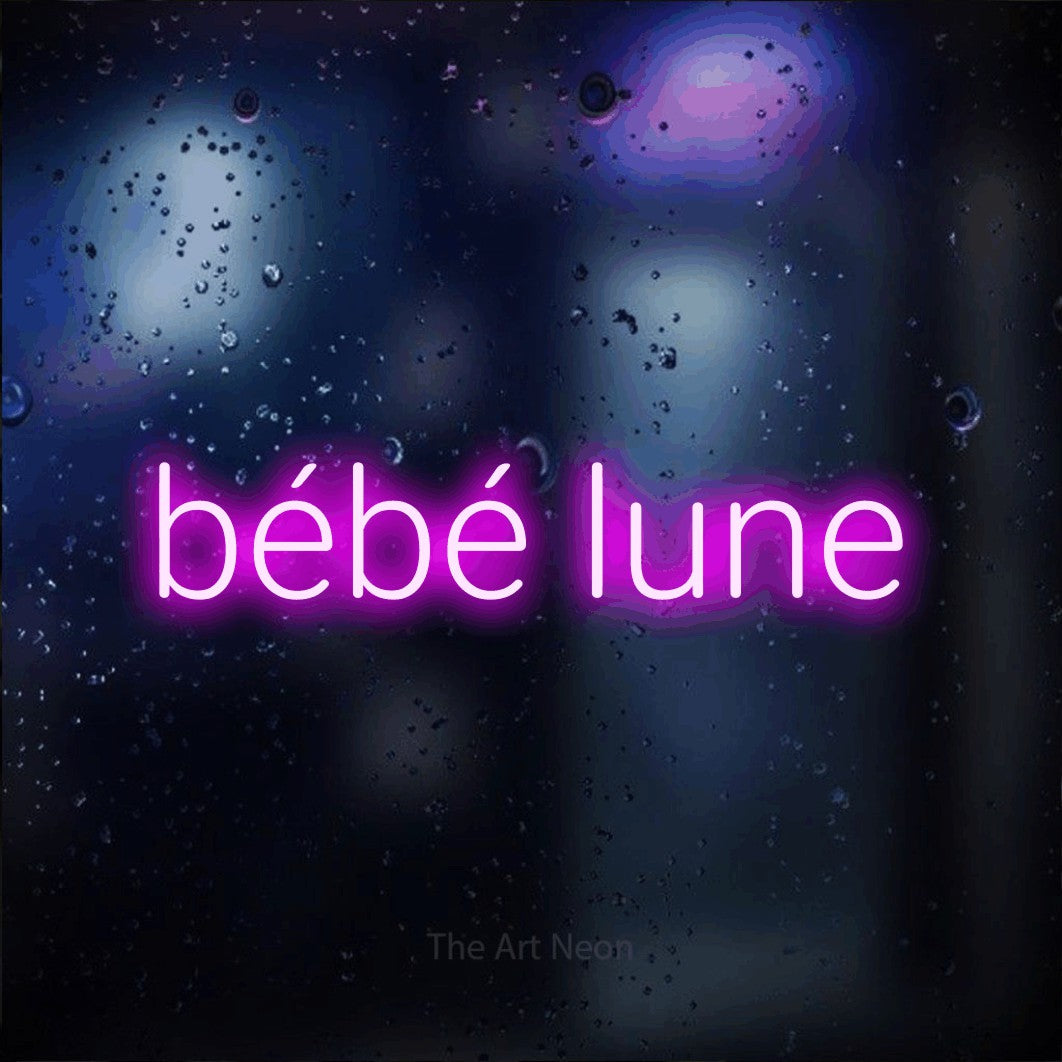 “Bébé lune” LED neon sign in pink, with rounded sans-serif lettering, shown against glass with blue and purple reflections.