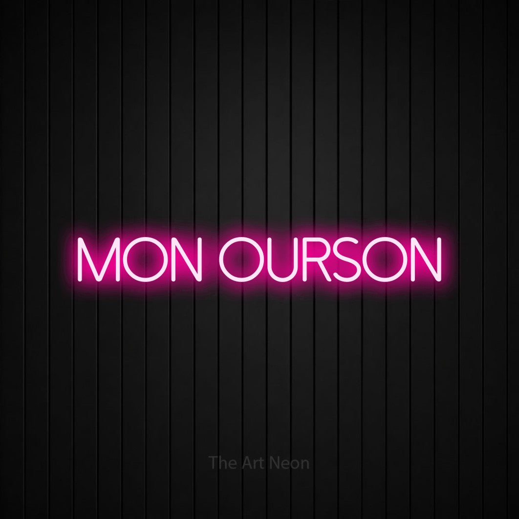 “Mon ourson” LED neon sign in hot pink, with thin sans-serif lettering, shown against black vertical wall slats.
