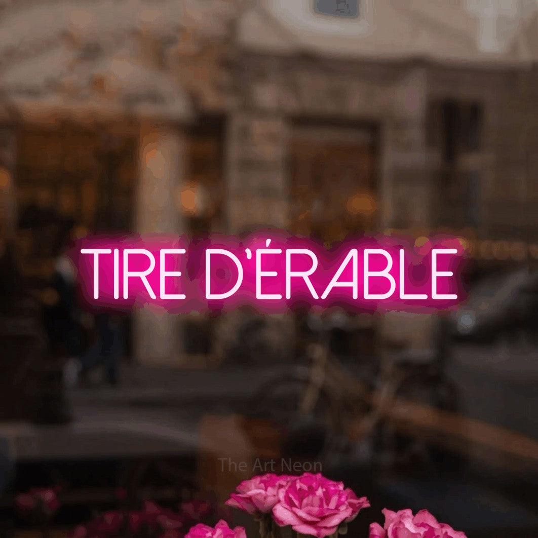“Tire d'érable” LED neon sign in hot pink, with thin sans-serif lettering, shown against a blurred café-bar interior.