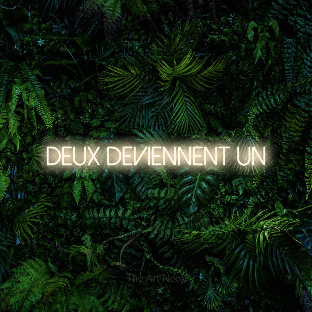 Lettrage en néon LED « Deux deviennent un » en blanc chaud, en lettres fines sans empattement, présenté devant un feuillage tropical dense, pour une réception de mariage.