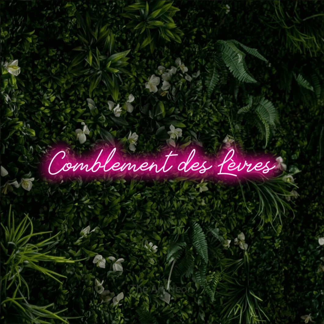 Décoration murale en néon LED « Comblement des lèvres » en rose vif, en lettrage cursif, installée sur un mur végétal vert et dense, pour un salon de beauté.