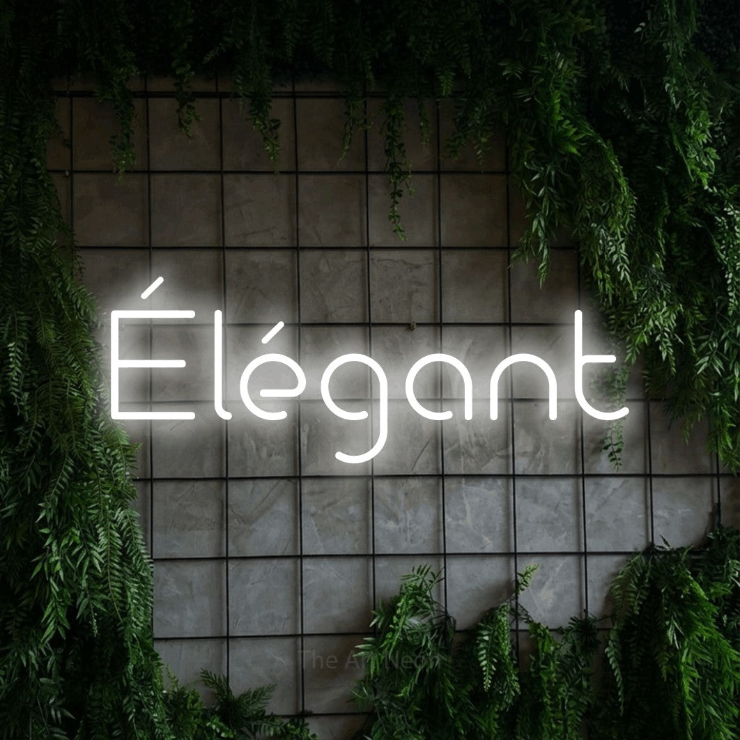 “Élégant” LED neon sign in cool white, with stylised geometric lettering, shown against an ivy-covered concrete grid.