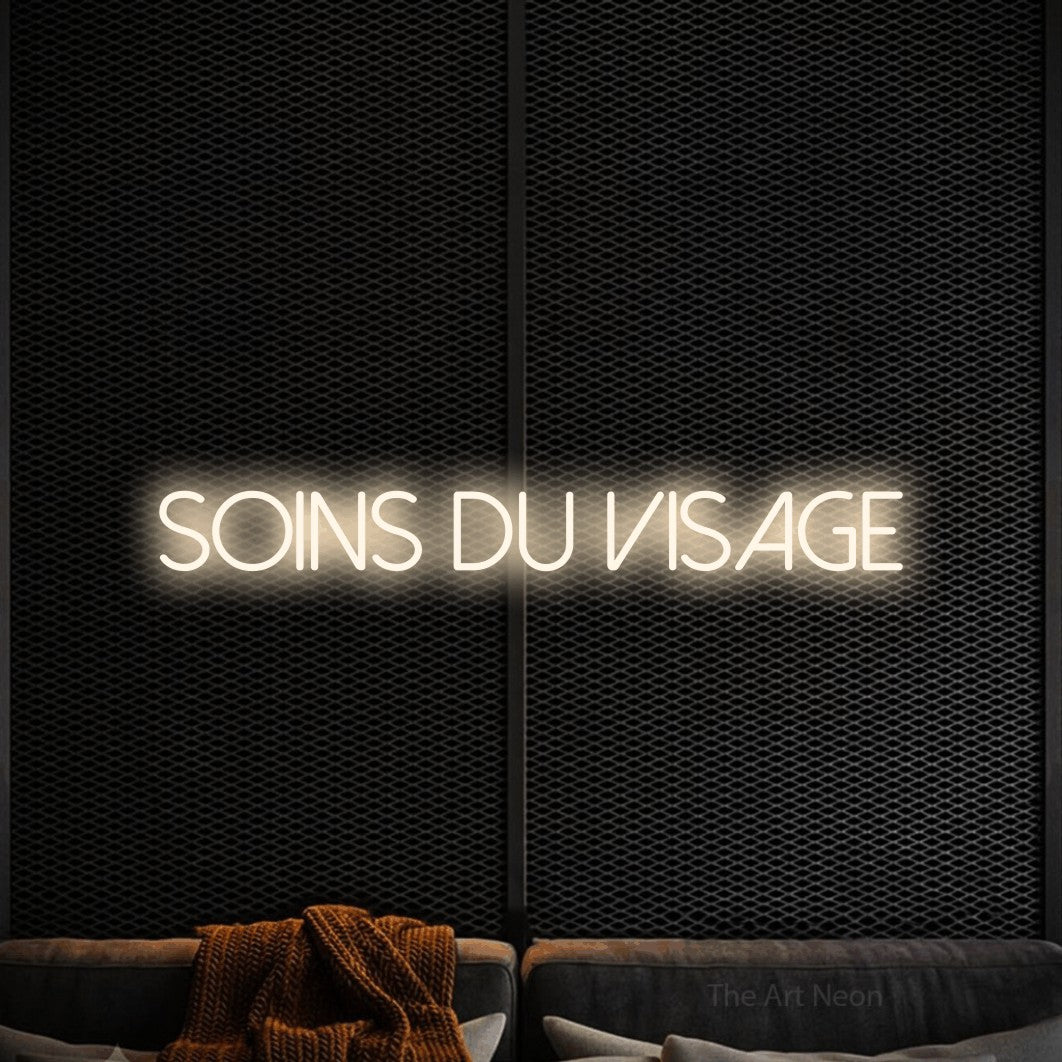 Néon LED « Soins du visage » en blanc chaud, en lettres fines sans empattement, mis en scène dans un coin salon moderne aux tons noirs, pour un salon de beauté.