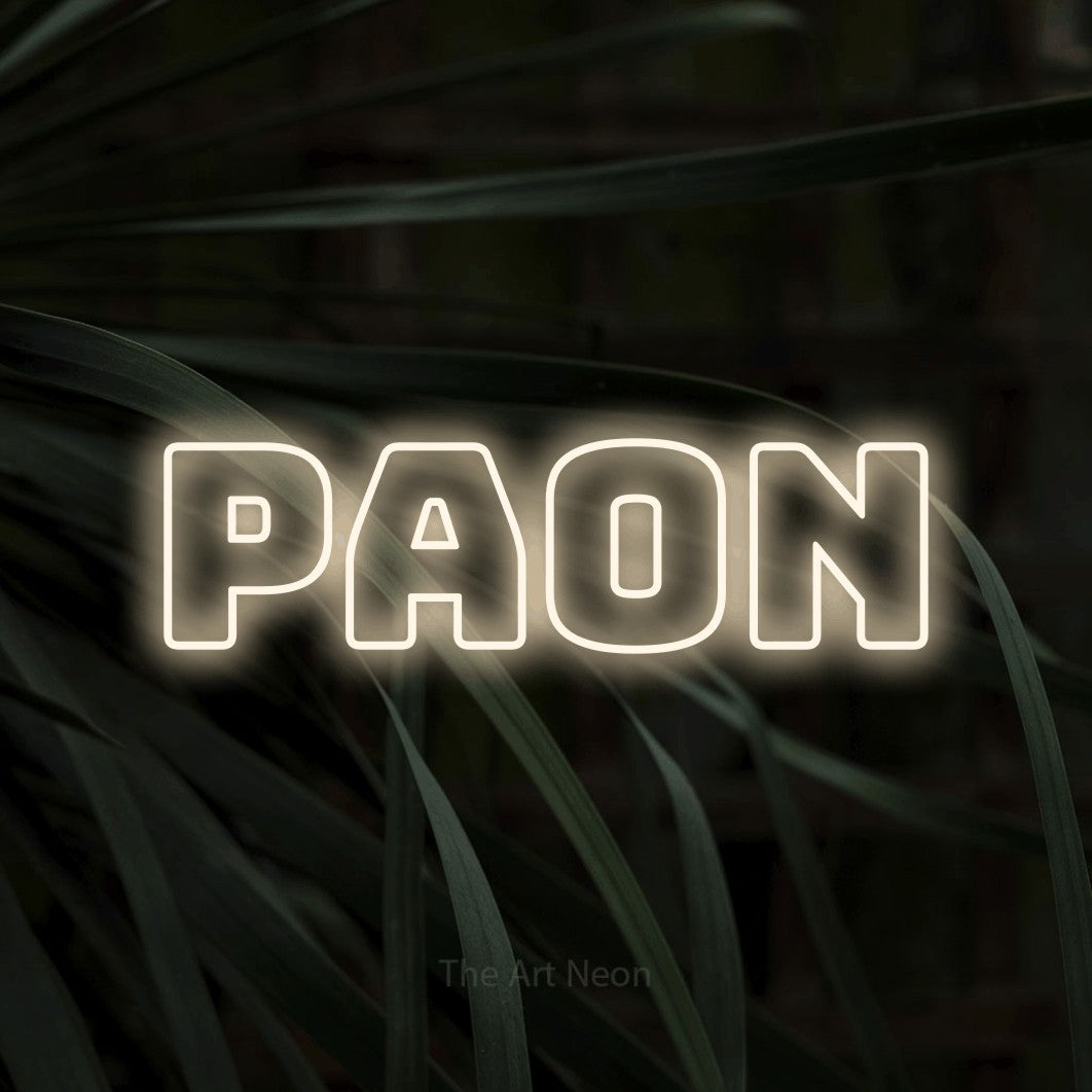 Composition en néon LED « Paon » en blanc chaud, en typographie contour épaisse, mise en valeur sur un feuillage sombre en gros plan, pour un décor inspiré de la nature.