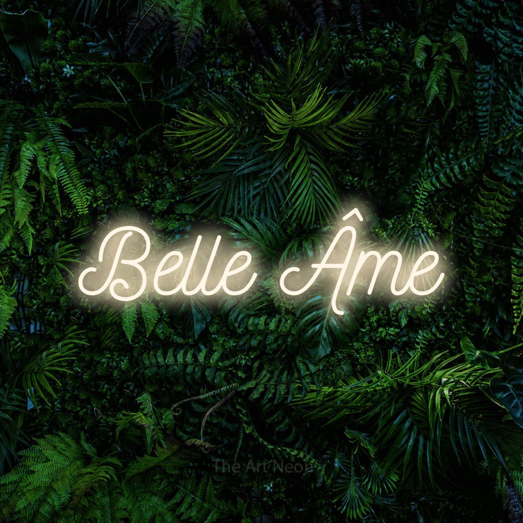 “Belle âme” LED neon sign in warm white, with ornate cursive lettering, shown against dense tropical foliage.