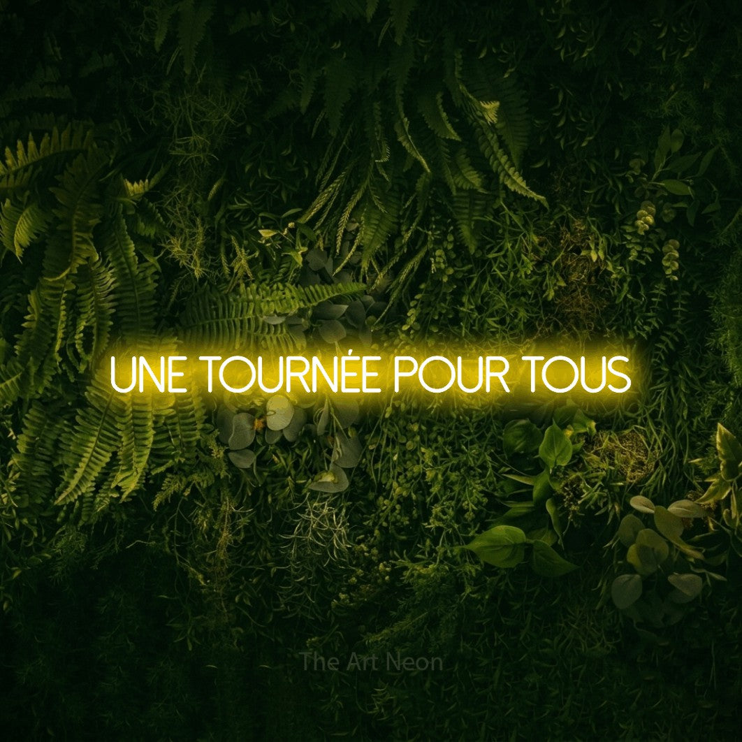 Néon LED « Une tournée pour tous » en jaune, en lettres fines sans empattement, mis en scène sur un fond sombre de mousse et de forêt, pour un bar ou un pub.