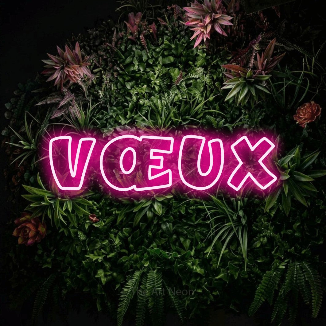 “Vœux” LED neon sign in hot pink, with rounded outline lettering, shown against a flowering plant wall.