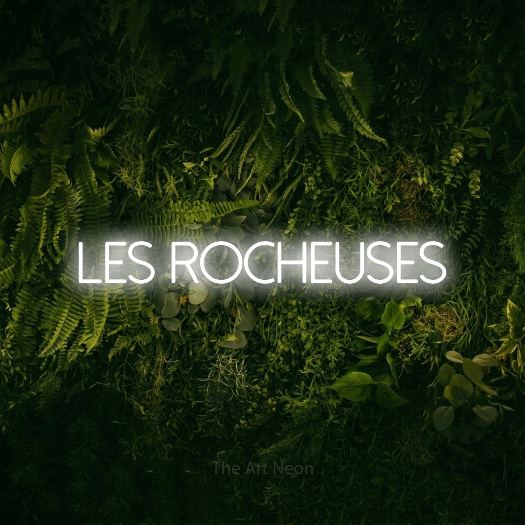 “Les rocheuses” LED neon sign in cool white, with thin sans-serif lettering, shown against a dark moss and forest backdrop.