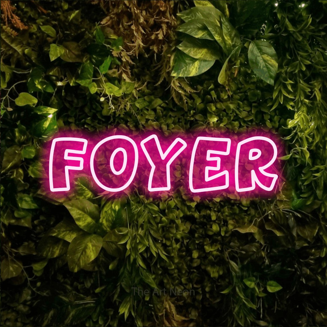 “Foyer” LED neon sign in hot pink, with rounded outline lettering, shown against bright green and yellow foliage.