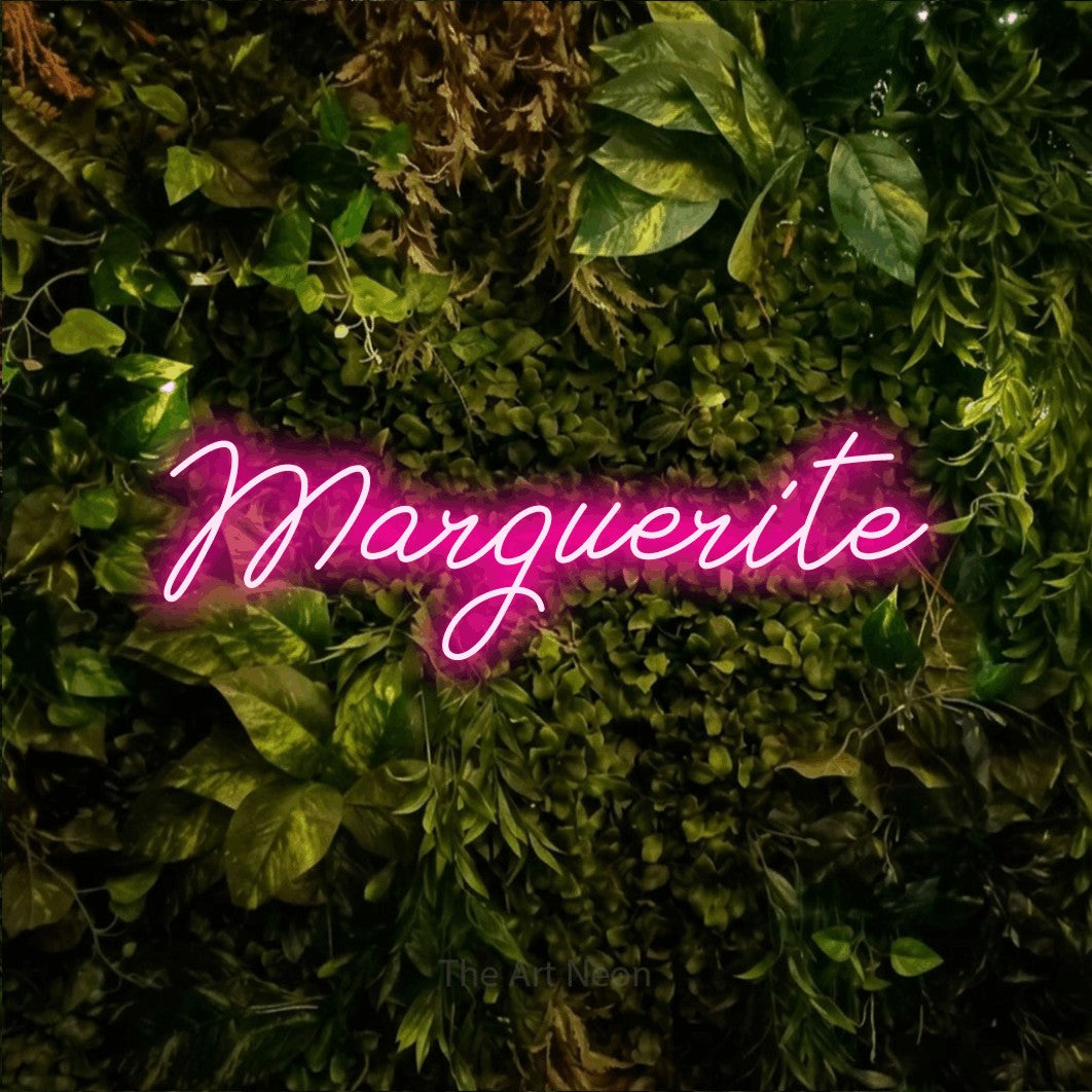 “Marguerite” LED neon sign in hot pink, with cursive lettering, shown against bright green and yellow foliage.