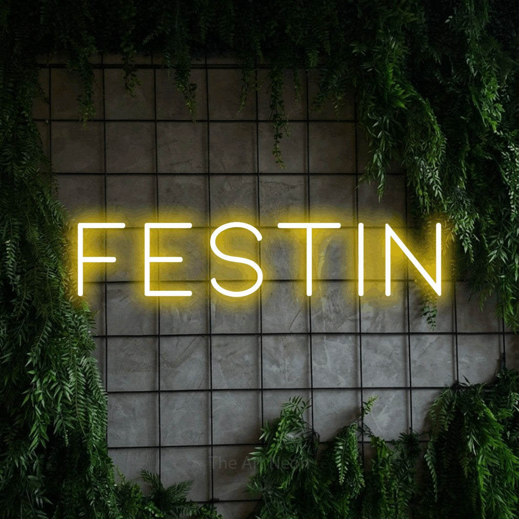 “Festin” LED neon sign in yellow, with thin, widely spaced lettering, shown against an ivy-covered concrete grid.