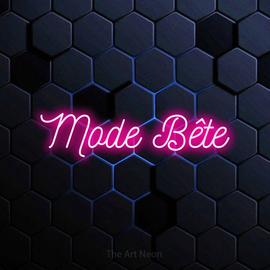 “Mode bête” LED neon sign in hot pink, with ornate cursive lettering, shown against a dark blue honeycomb pattern.