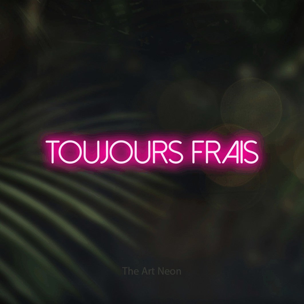 “Toujours frais” LED neon sign in hot pink, with thin sans-serif lettering, shown against a blurred palm and bokeh-light backdrop.