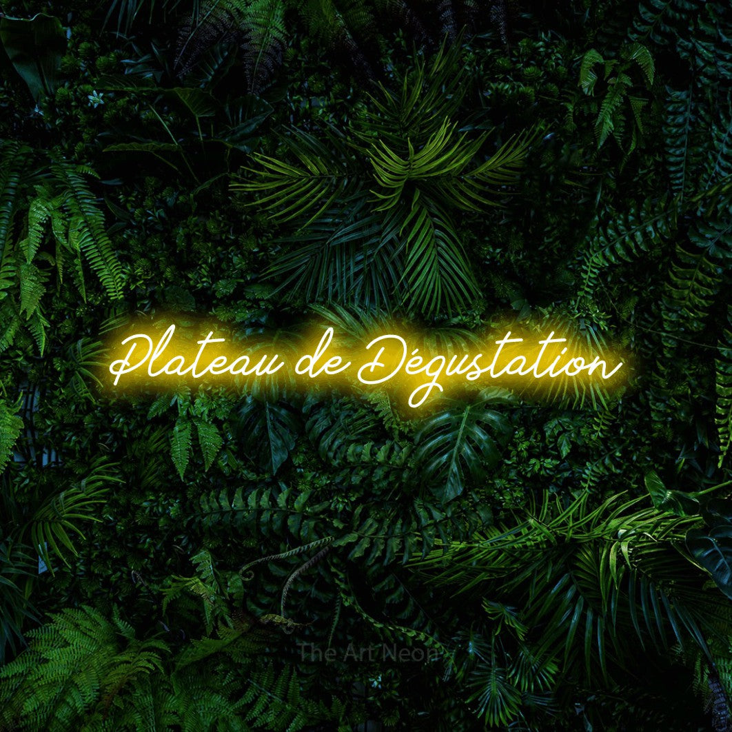 “Plateau de dégustation” LED neon sign in yellow, with cursive lettering, shown against dense tropical foliage.