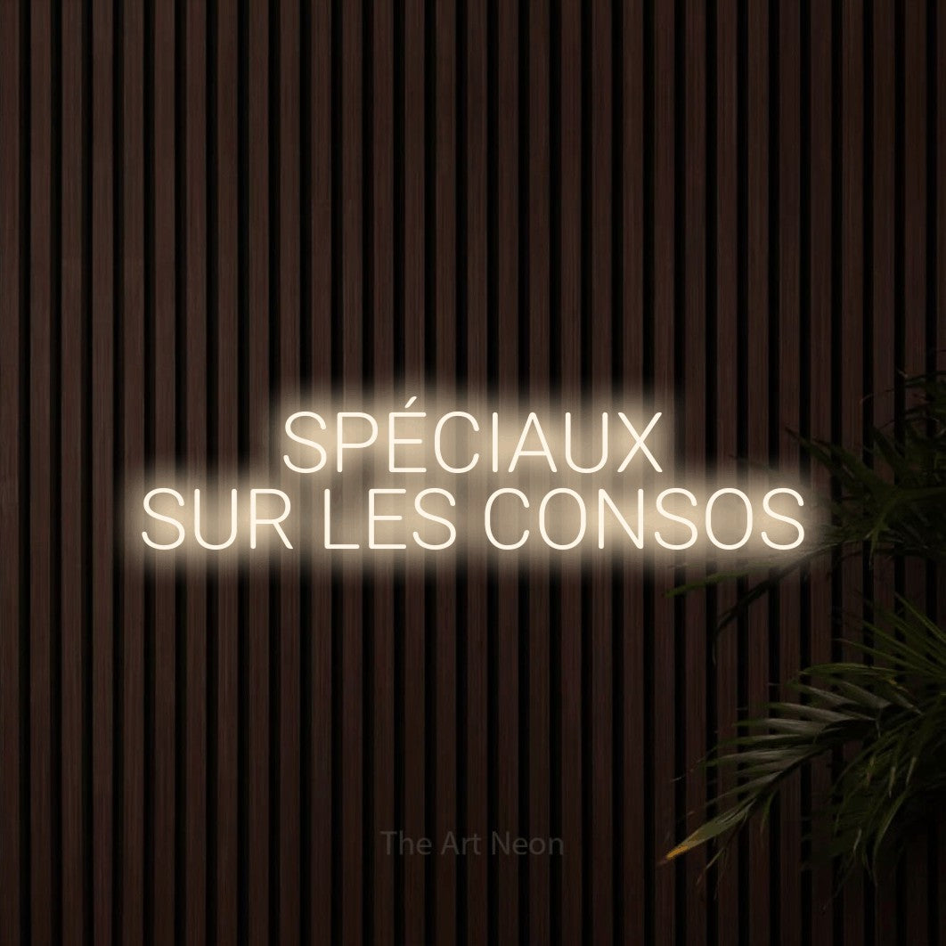 “Spéciaux sur les consos” LED neon sign in warm white, with rounded sans-serif lettering across 2 lines, shown against dark wooden wall slats.