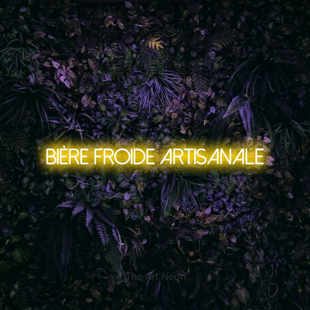 “Bière froide artisanale” LED neon sign in yellow, with thin sans-serif lettering, shown against a dark wall with purple flowers.