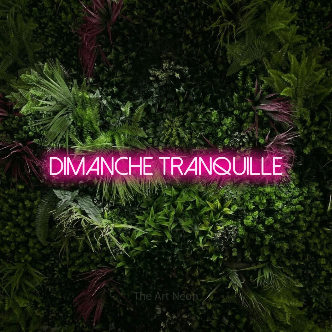 “Dimanche tranquille” LED neon sign in hot pink, with thin sans-serif lettering, shown against a plant wall with pink flowers.