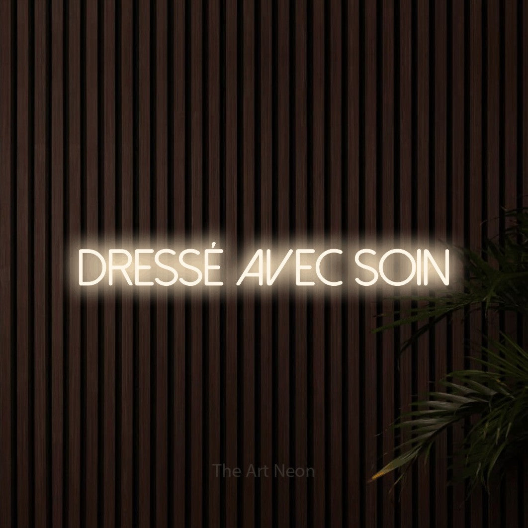 “Dressé avec soin” LED neon sign in warm white, with thin sans-serif lettering, shown against dark wooden wall slats.