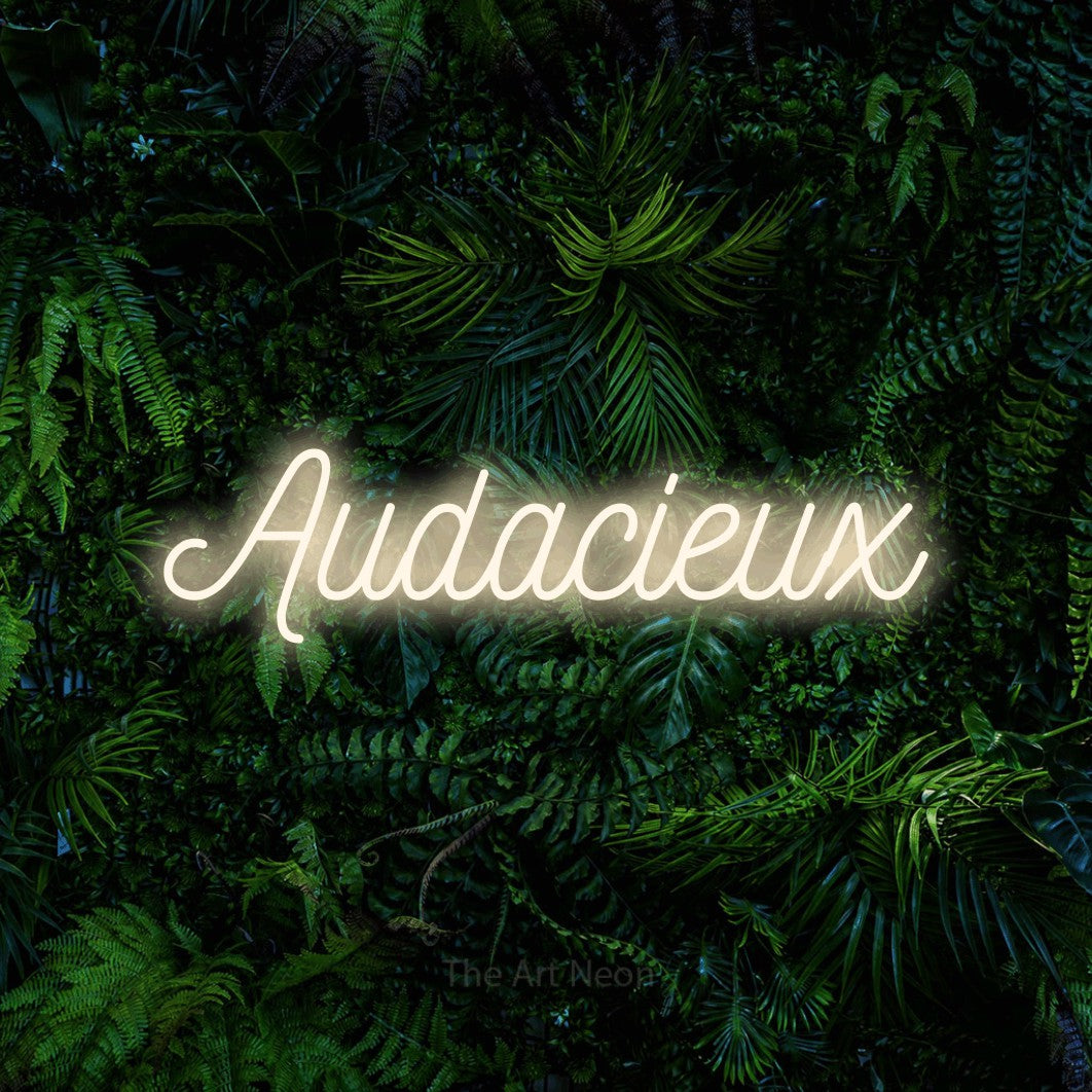 “Audacieux” LED neon sign in warm white, with ornate cursive lettering, shown against dense tropical foliage.