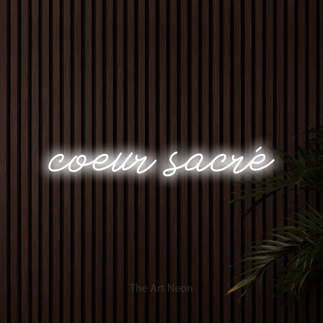 “Cœur sacré” LED neon sign in cool white, with cursive lettering, shown against dark wooden wall slats.