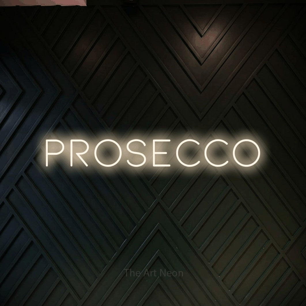 “Prosecco” LED neon sign in warm white, with thin, widely spaced lettering, shown against a black chevron-patterned wood wall.