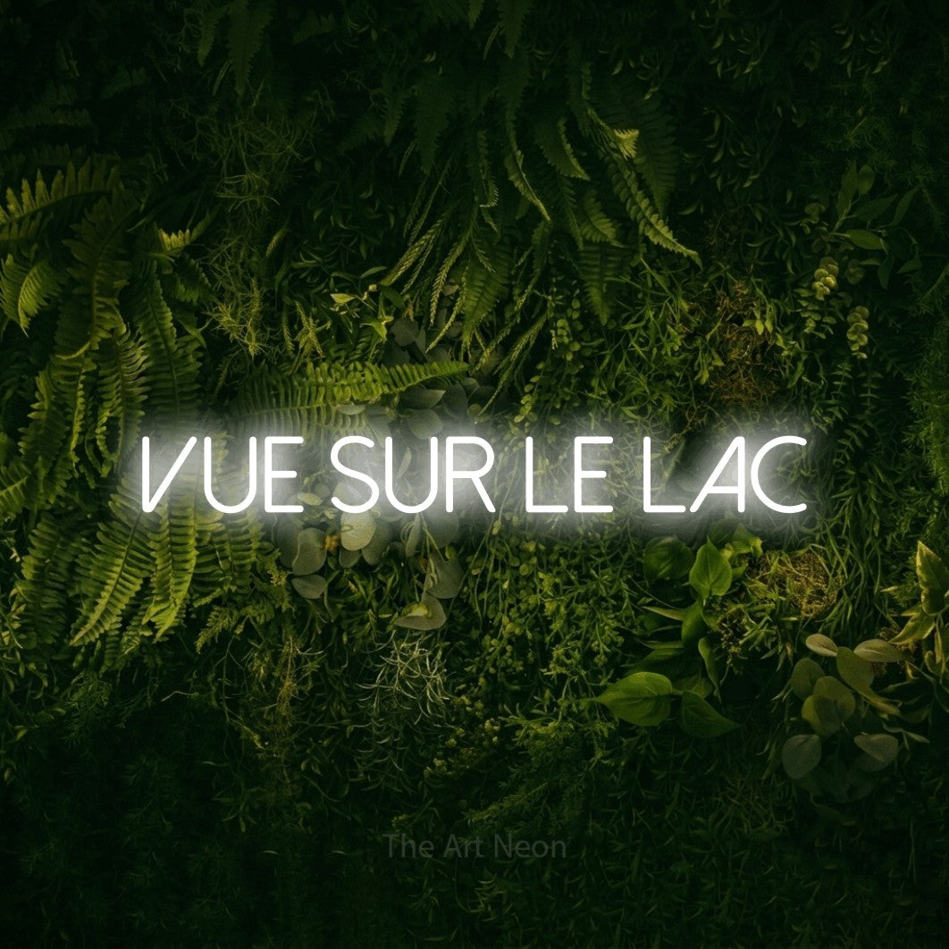 “Vue sur le lac” LED neon sign in cool white, with thin sans-serif lettering, shown against a dark moss and forest backdrop.