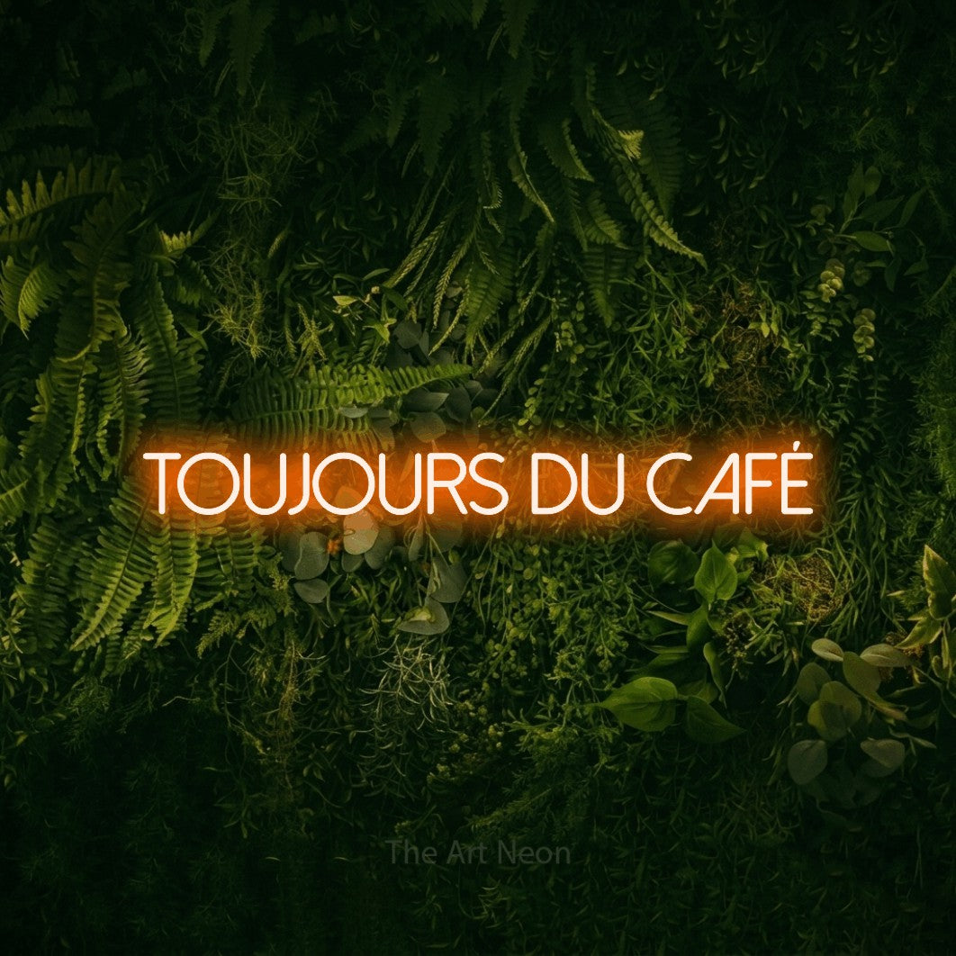 Lettrage en néon LED « Toujours du café » en orange, en lettres fines sans empattement, présenté sur un fond sombre de mousse et de forêt, pour un café.