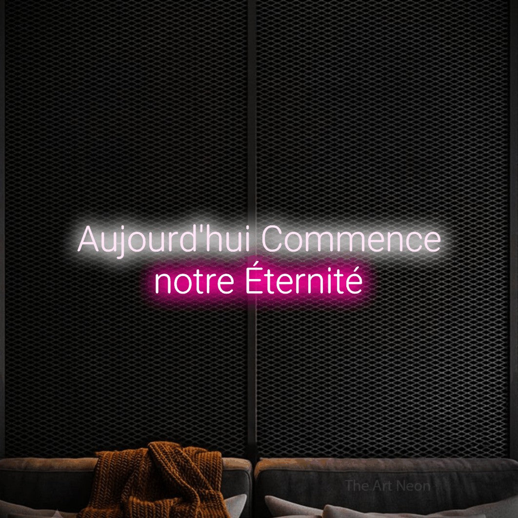 “Aujourd'hui commence notre éternité” LED neon sign in cool white on the upper line and hot pink on the lower line, with rounded sans-serif lettering across 2 lines, shown against a modern dark-toned seating area.