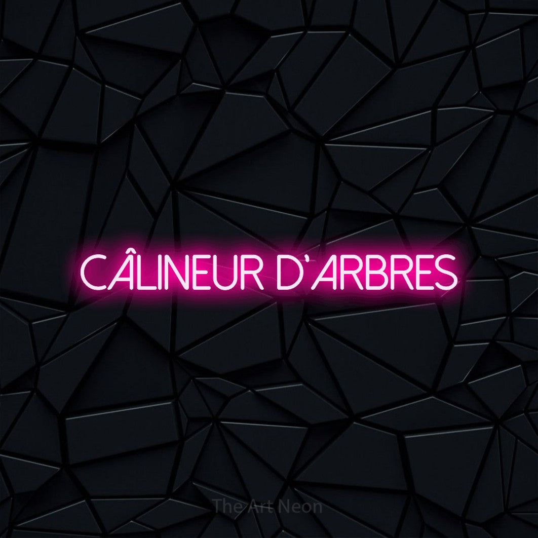 “Câlineur d'arbres” LED neon sign in hot pink, with thin sans-serif lettering, shown against a black polygonal surface.