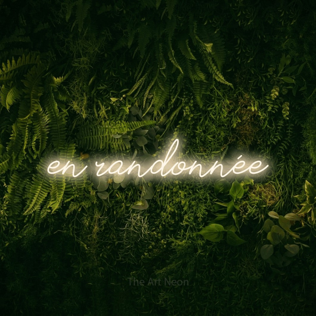 “En randonnée” LED neon sign in warm white, with cursive lettering, shown against a dark moss and forest backdrop.