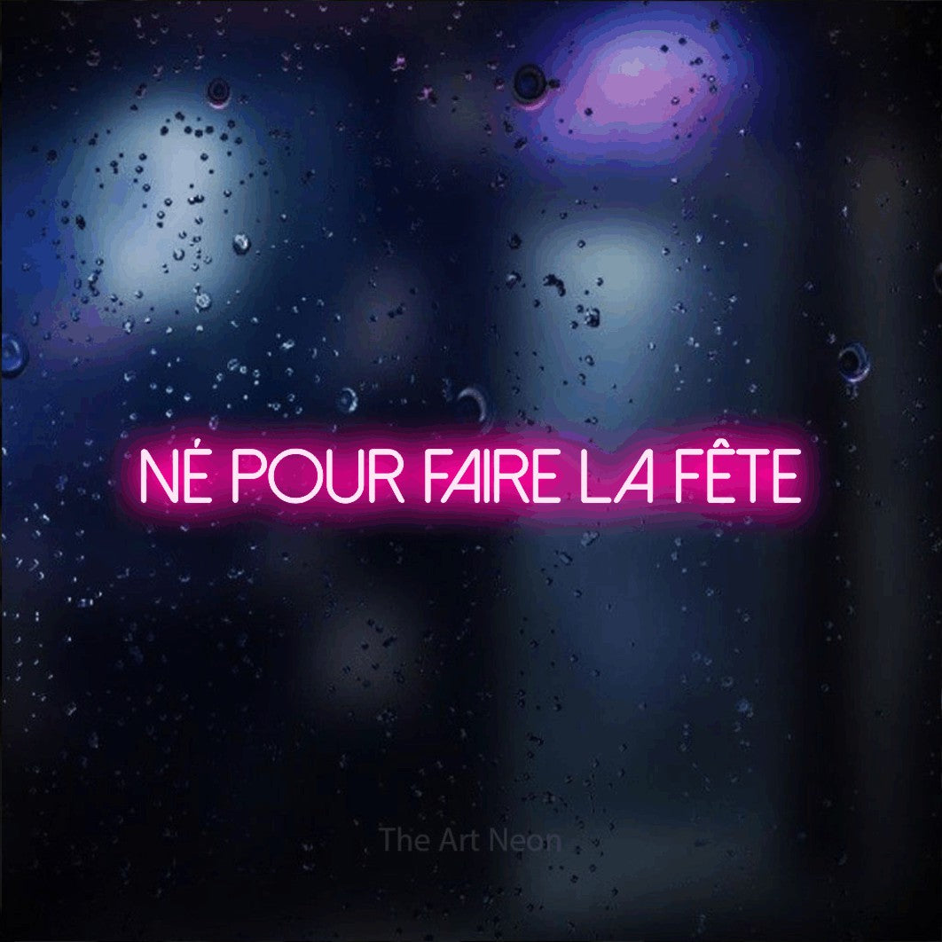 Lettrage en néon LED « Né pour faire la fête » en rose vif, en lettres fines sans empattement, présenté sur une vitre aux reflets bleus et violets, pour une fête.