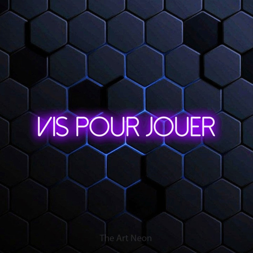 “Vis pour jouer” LED neon sign in purple, with thin sans-serif lettering, shown against a dark blue honeycomb pattern.